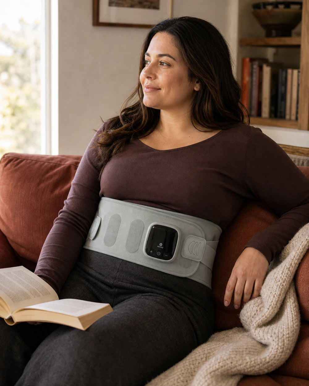Woman relaxing at home while wearing ESCOSY Lumbar One with its integrated control panel fixed to the wrap